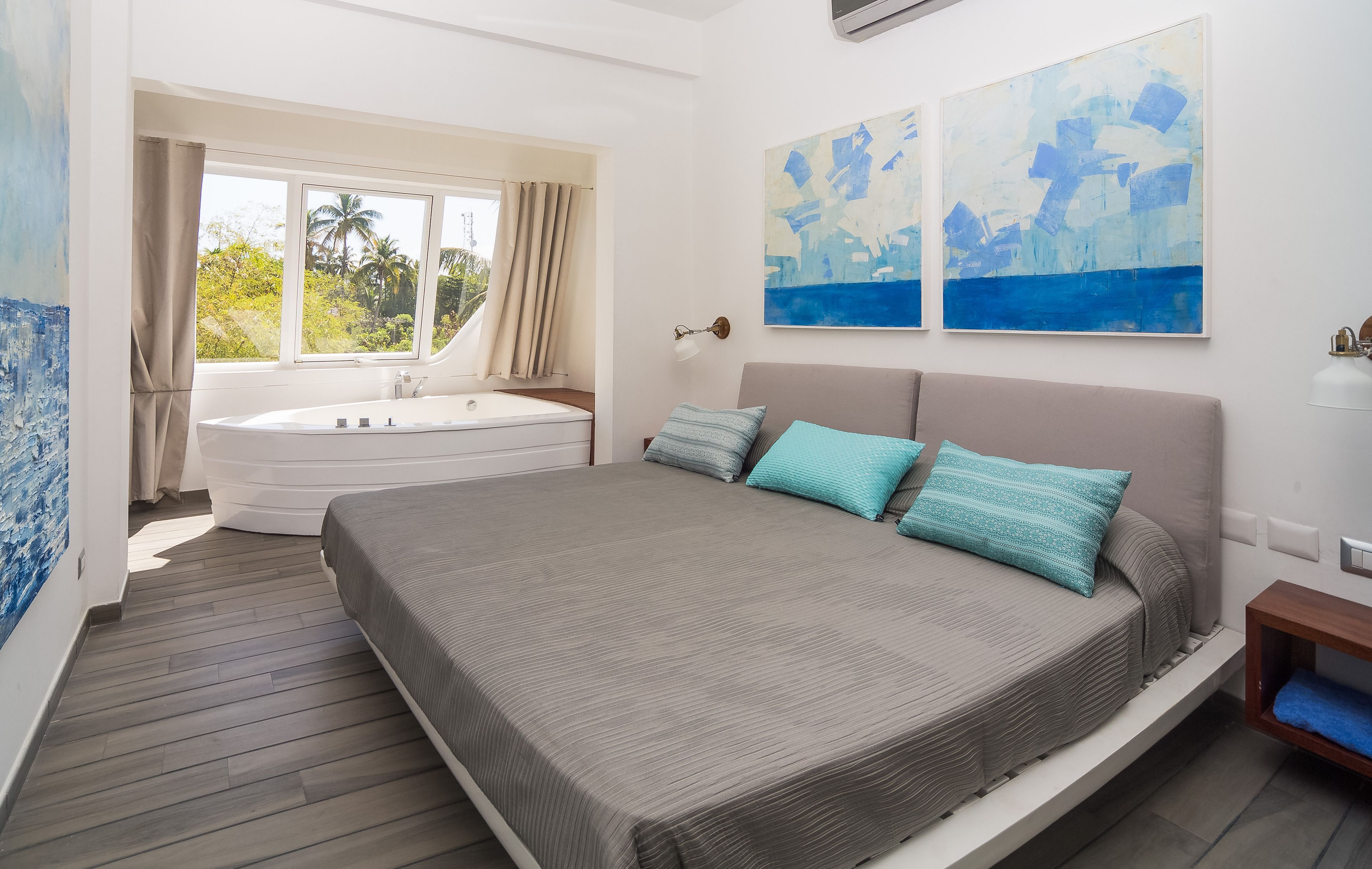 A bedroom with a large bed, a bathtub, and two abstract paintings on the wall.