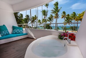 A balcony with a white bathtub, teal patterned cushions, and a view of the beach and palm trees. - Puerto Plaza Las Terrenas (Las Terrenas)