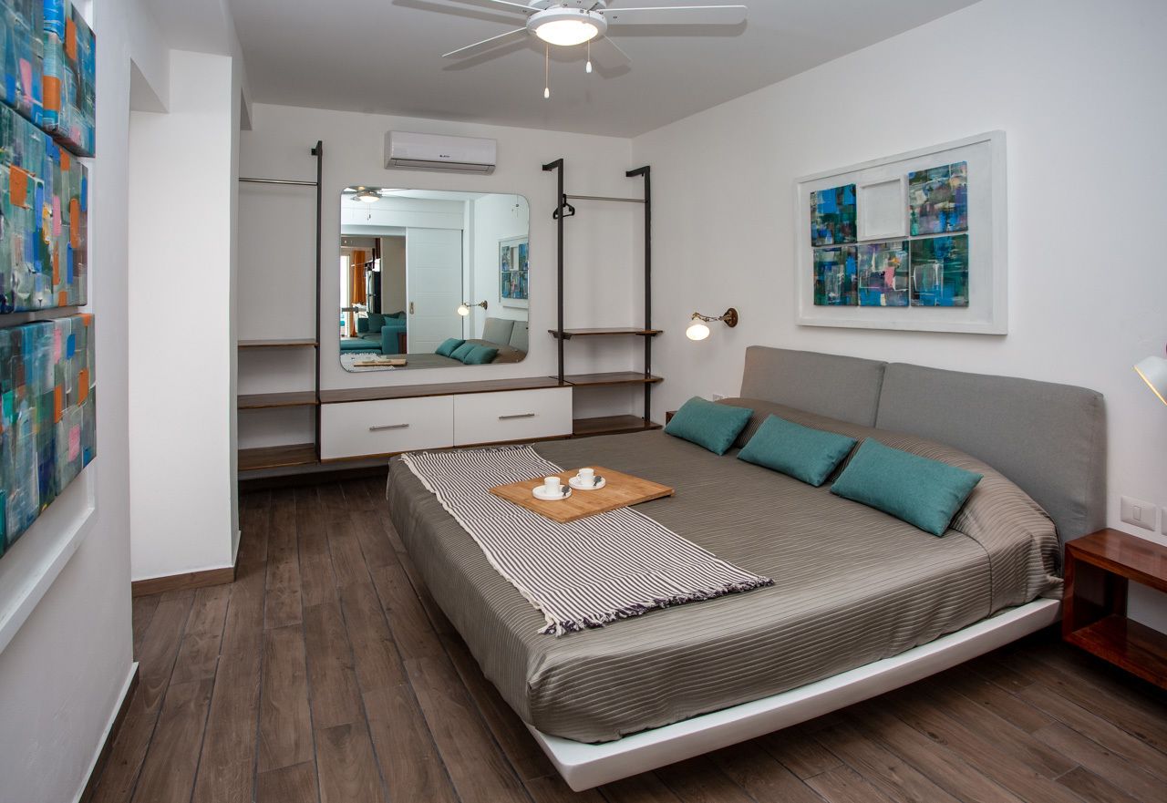 Un dormitorio moderno con una cama, un ventilador de techo, un espejo grande y obras de arte en las paredes.