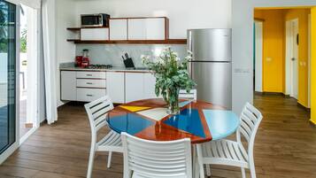A modern kitchen with white cabinets, a stainless steel refrigerator, and a dining area with a colorful table and white chairs.