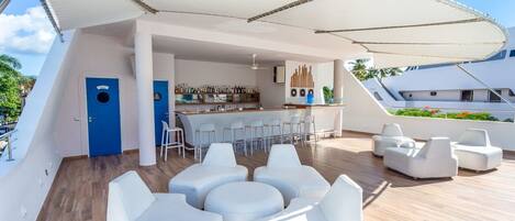 Un'area salotto esterna moderna con poltrone bianche e un bar con bancone bianco e sgabelli.