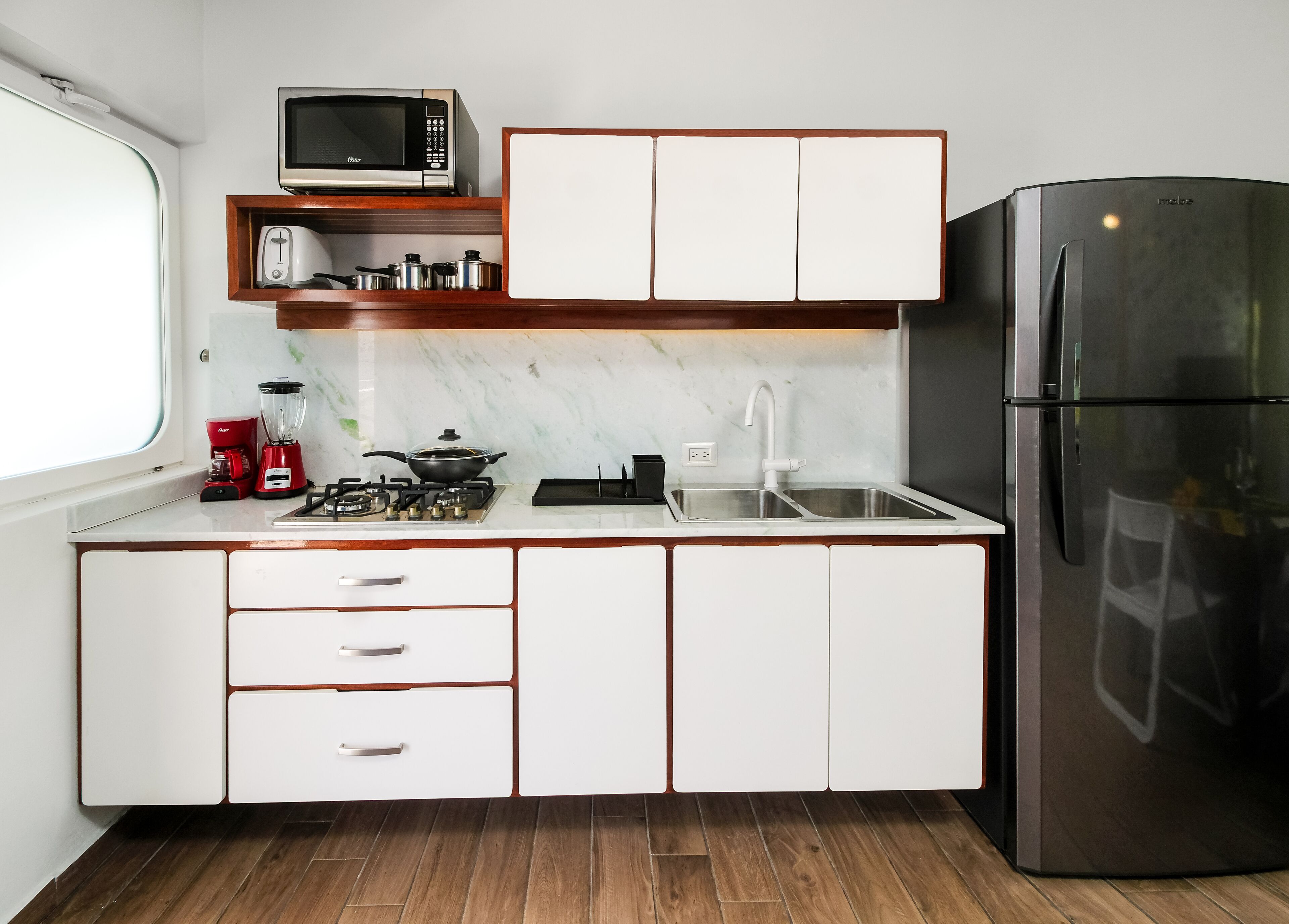 A modern kitchen with white cabinets, a stainless steel refrigerator, a microwave, a stove, and a sink.