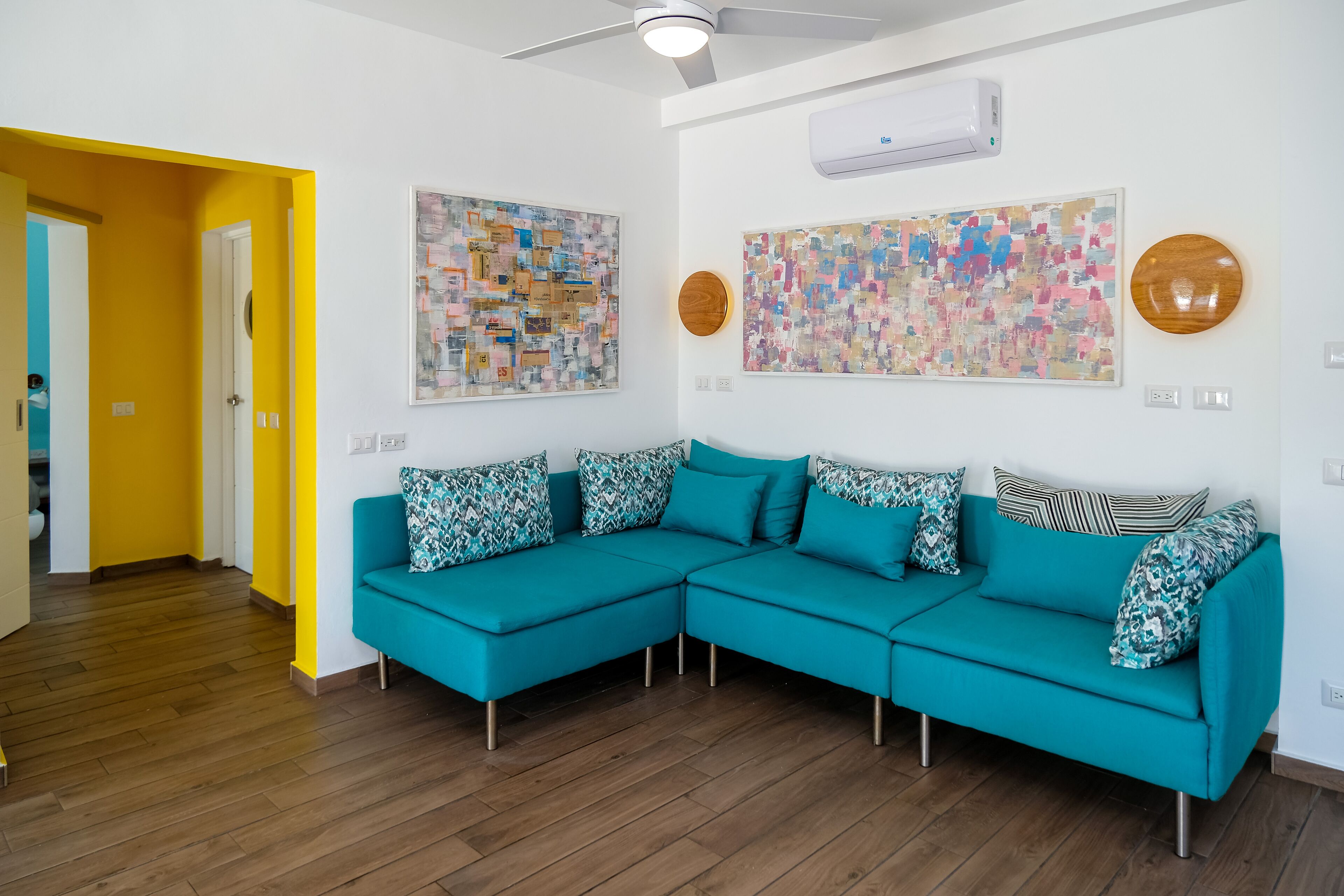 A modern living room with a teal sectional sofa, two abstract paintings, and a wooden accent wall.