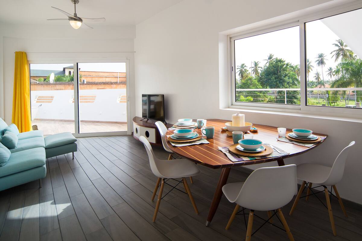 A modern dining area with a wooden table set for four, white chairs, and a television on a stand.