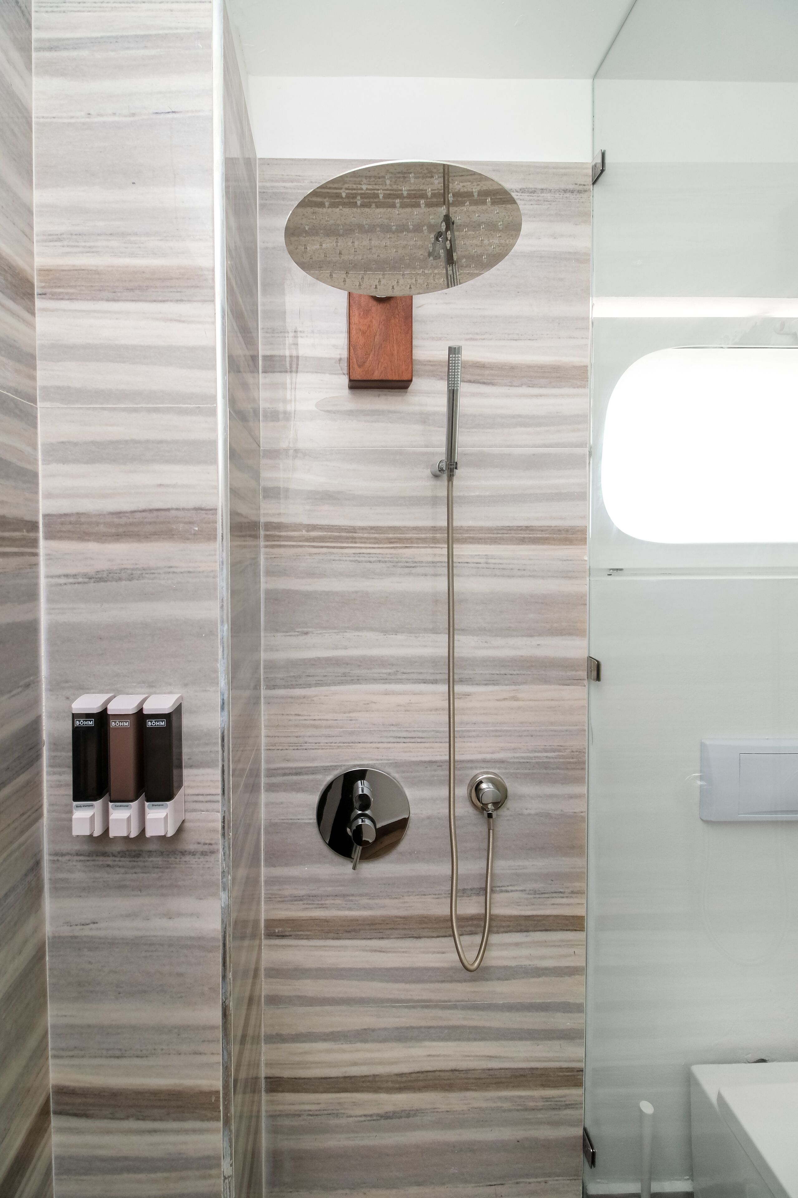 A modern bathroom with a shower, a wooden panel above the shower, and a glass door.