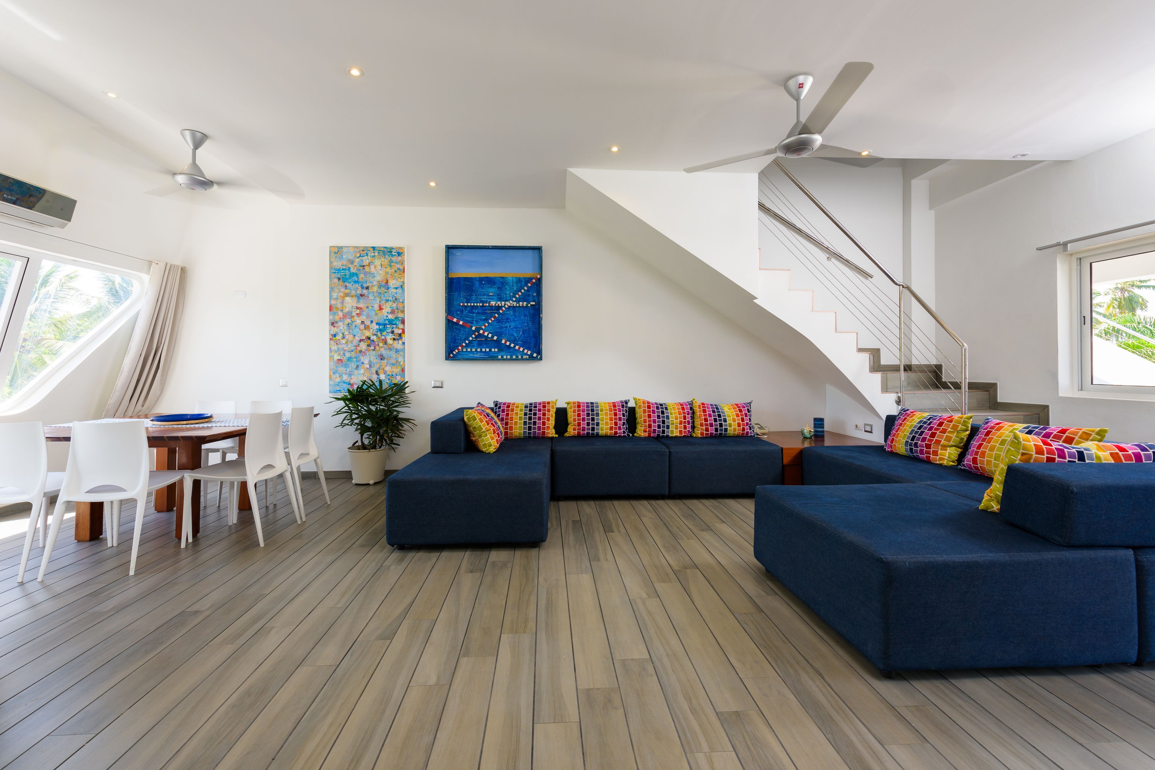 A modern living room with a sectional sofa, a dining table with chairs, and a staircase.