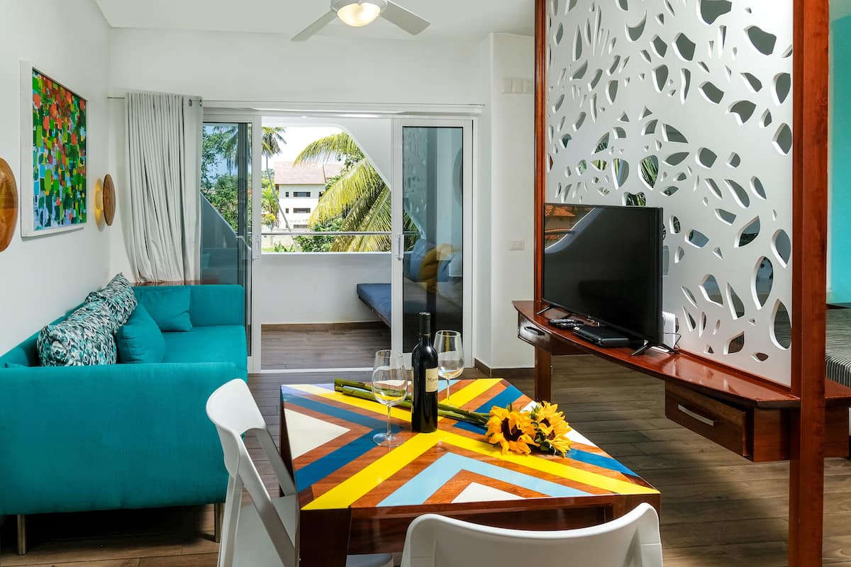 A modern living room with a teal sofa, a colorful table, and a TV on a wooden stand.
