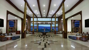 A spacious lobby with a central seating area, large windows offering a view of the mountains, and a modern design with wooden beams and a polished floor.