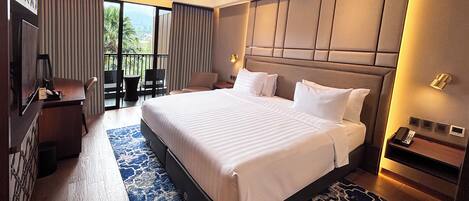 A hotel room with a large bed, a desk, a chair, and a balcony with a view.