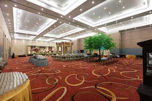 Un amplio salón de banquetes con alfombra roja, filas de sillas, un arreglo floral central y un gran árbol.