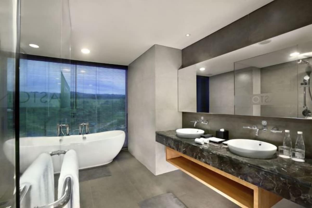 A modern bathroom with a freestanding bathtub, two sinks, and a large mirror.