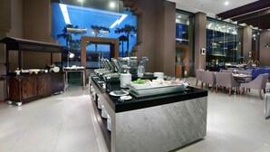 A modern hotel lobby with a buffet area, seating, and a large window with a view of palm trees.