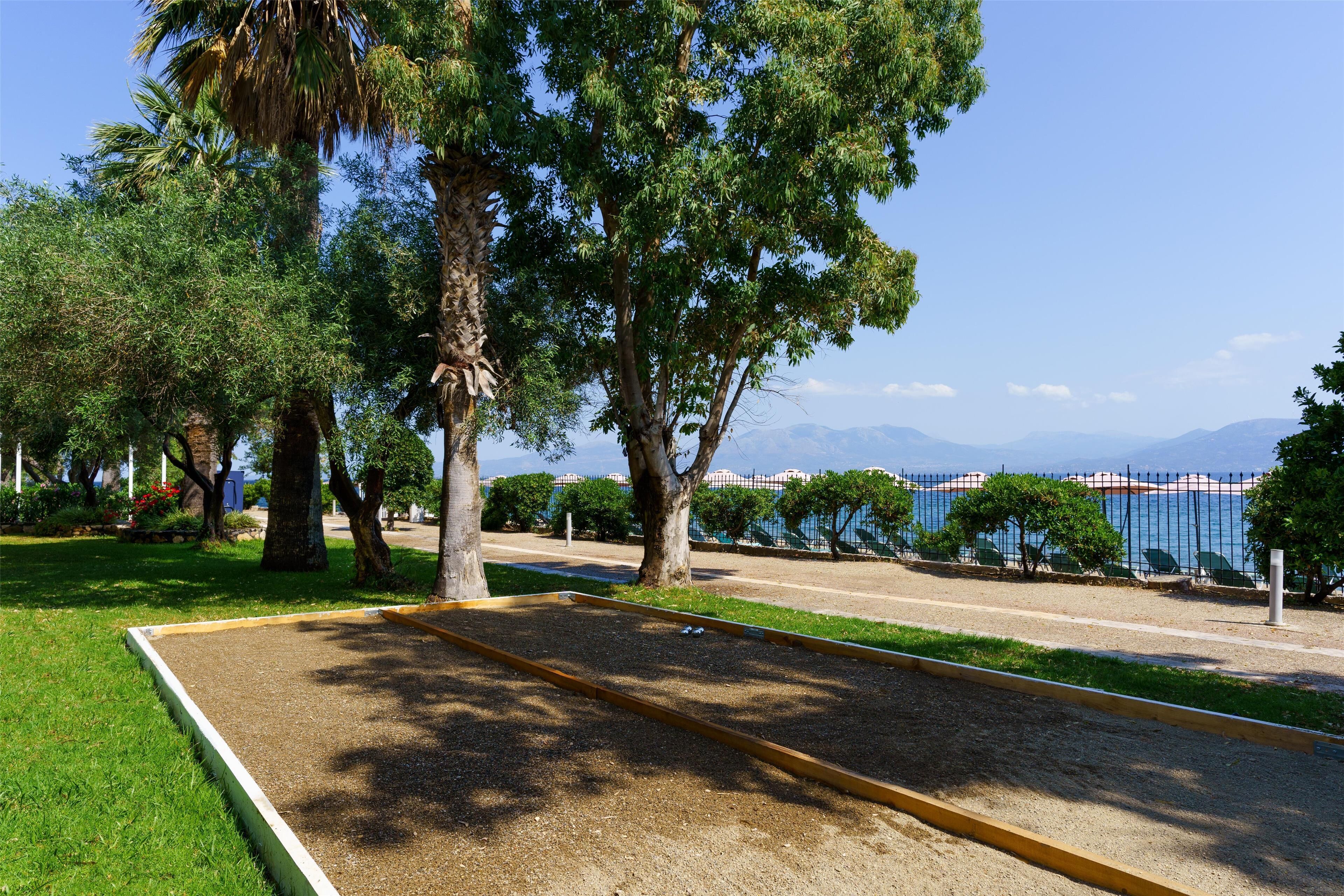 Ein Park mit Sandkasten, Bäumen, einem Zaun und einem Gewässer im Hintergrund.