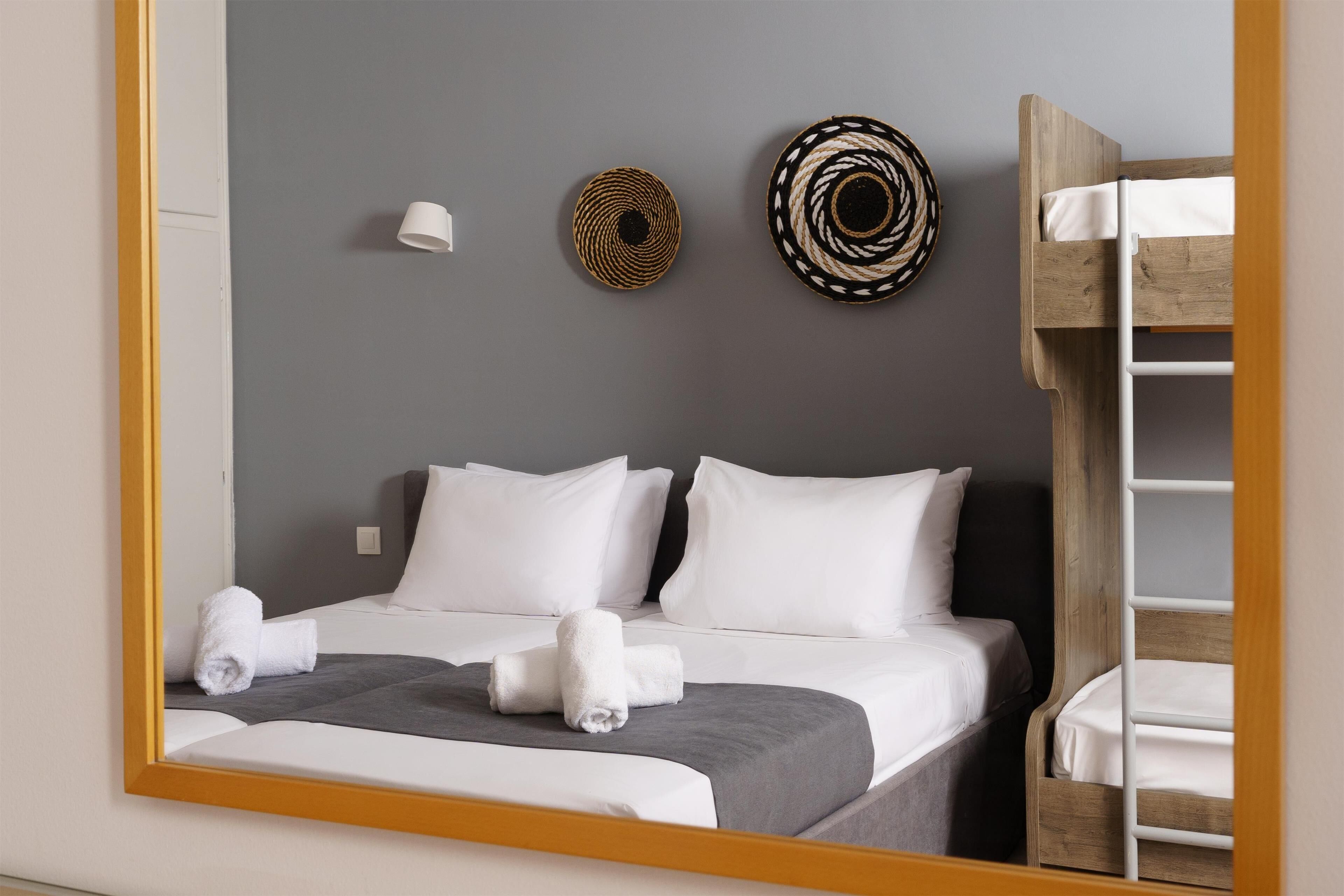 Habitación de hotel con cama, espejo, lámpara fijada a la pared y dos adornos textiles en la pared.