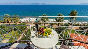 A balcony with a table set with fruit and wine glasses, overlooking a beach and the sea. - Calamos Beach Hotel by Anayia All Inclusive Resorts (Oropos)