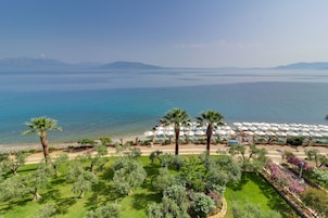 A coastal hotel with a view of the sea, palm trees, and a garden area with umbrellas.