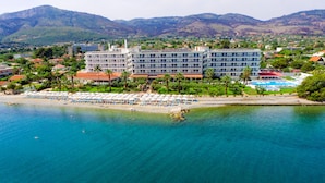 A coastal hotel with multiple floors, a beach with umbrellas, and a mountainous backdrop. - Calamos Beach Hotel by Anayia All Inclusive Resorts (Oropos)