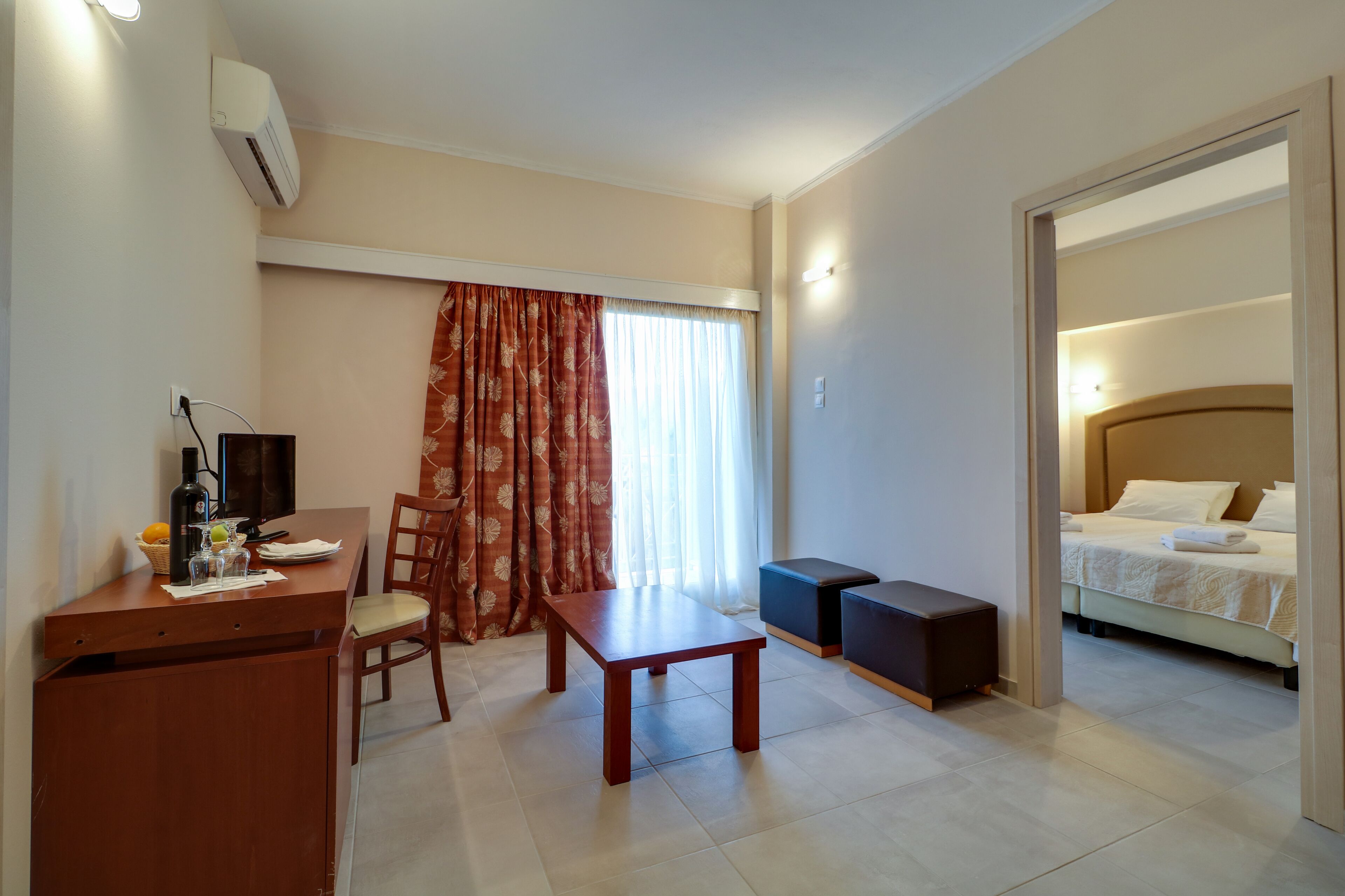 Quarto de hotel com escrivaninha de madeira, uma cadeira, uma mesinha, cama e guarda-roupa.