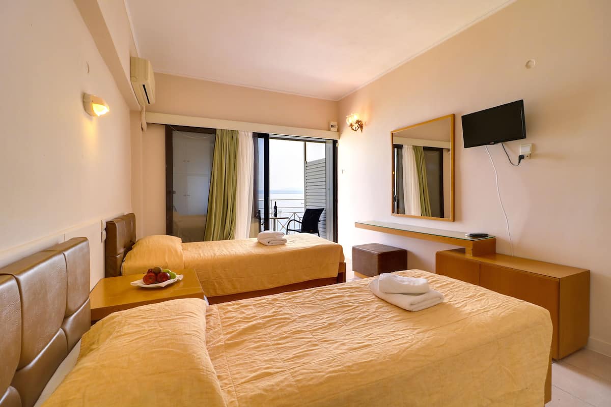 A hotel room with two beds, a desk, a TV, and a balcony with curtains.