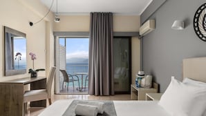 A hotel room with a bed, a desk, a chair, a view of the ocean, and a balcony with a curtain. - Calamos Beach Hotel by Anayia All Inclusive Resorts (Oropos)