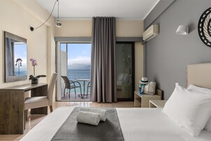 A hotel room with a bed, a desk, a chair, a view of the ocean, and a balcony with a curtain.