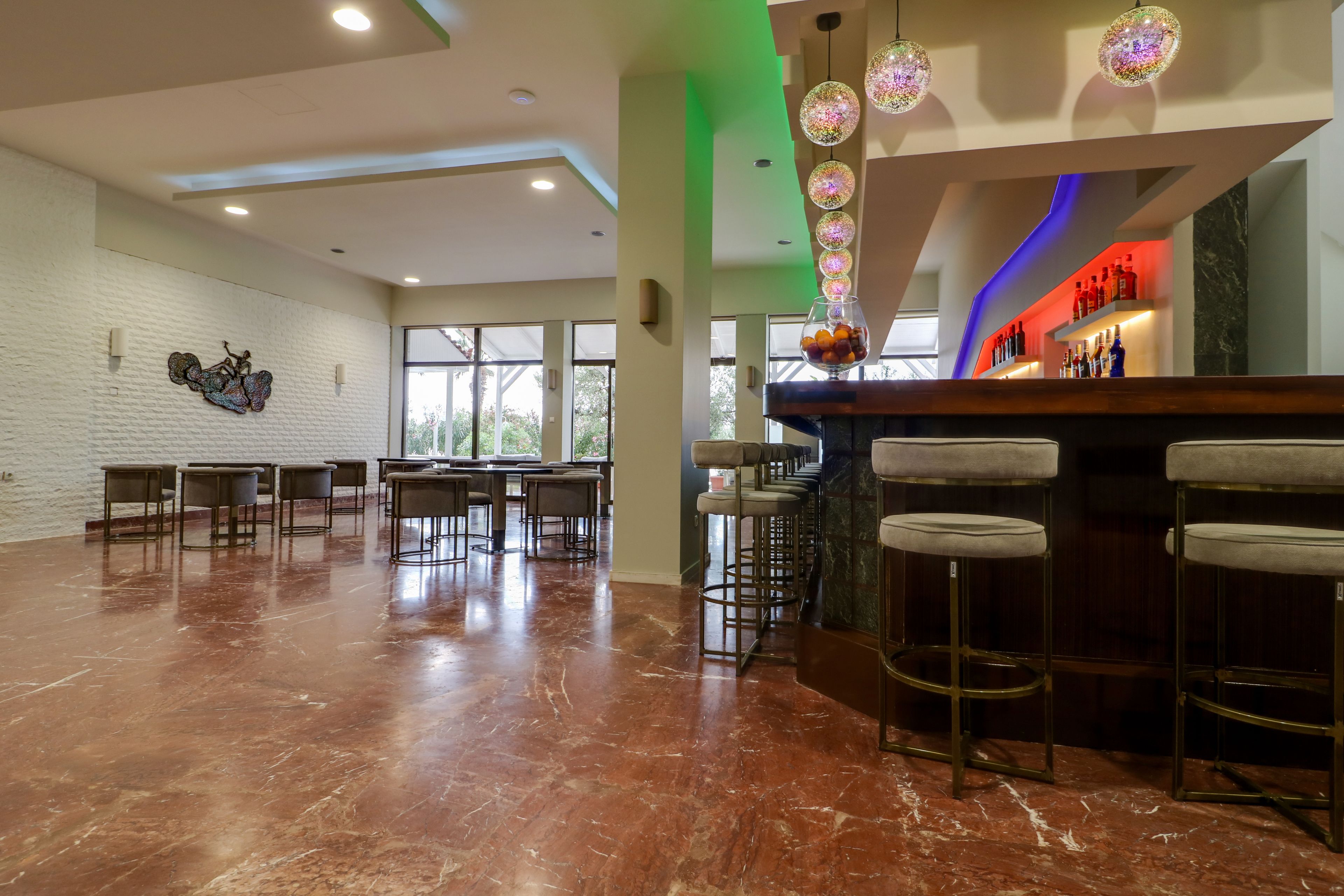 A modern bar area with a polished marble floor, a bar counter with stools, and decorative hanging lights.