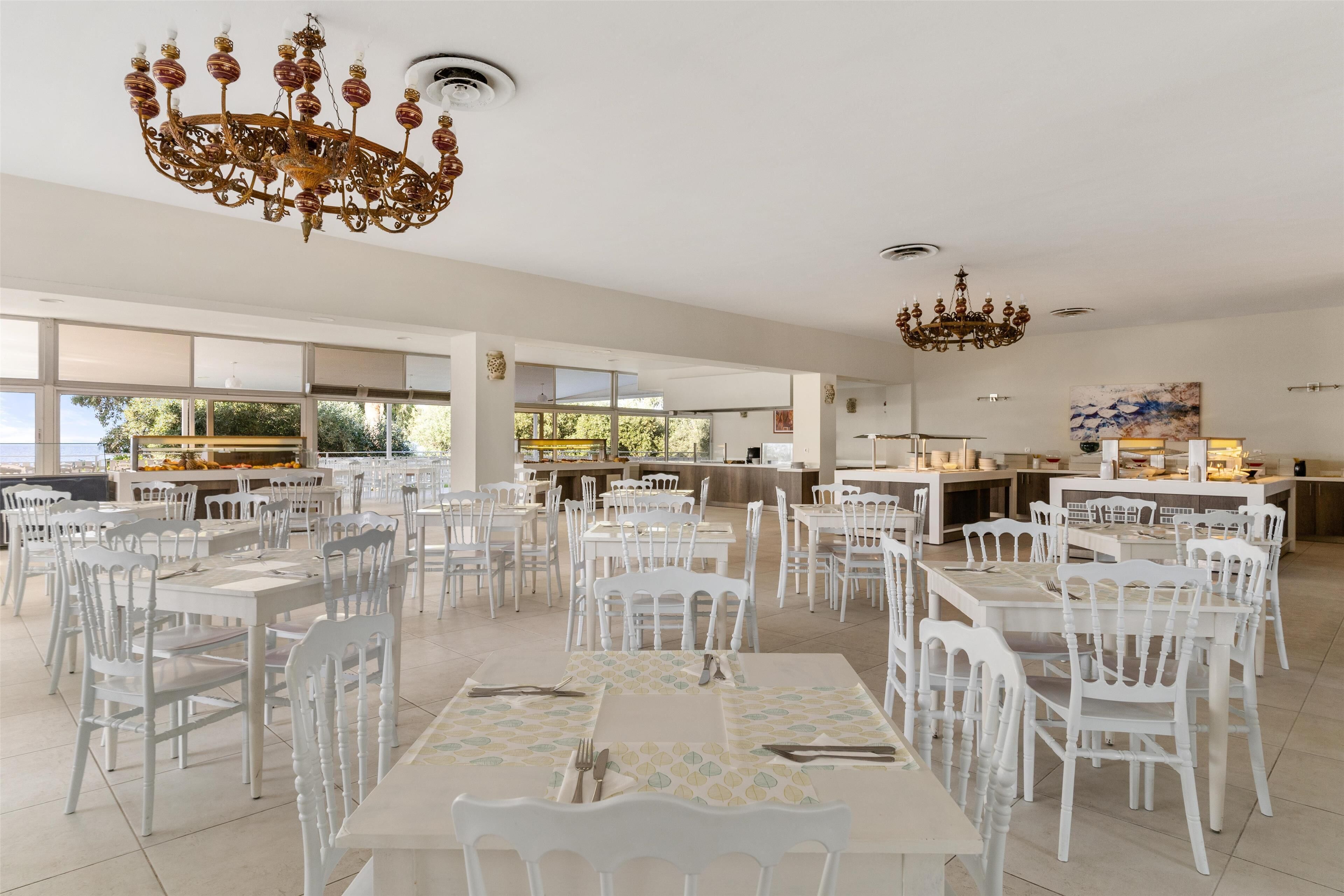Un comedor amplio con mesas y sillas blancas, candelabros y vistas al exterior.