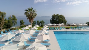 A pool area with blue lounge chairs and white umbrellas, overlooking a body of water with mountains in the distance. - Calamos Beach Hotel by Anayia All Inclusive Resorts (Oropos)