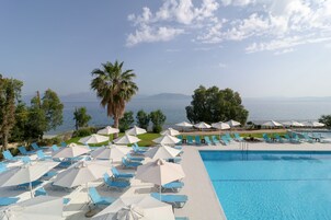 A pool area with blue lounge chairs and white umbrellas, overlooking a body of water with mountains in the distance.