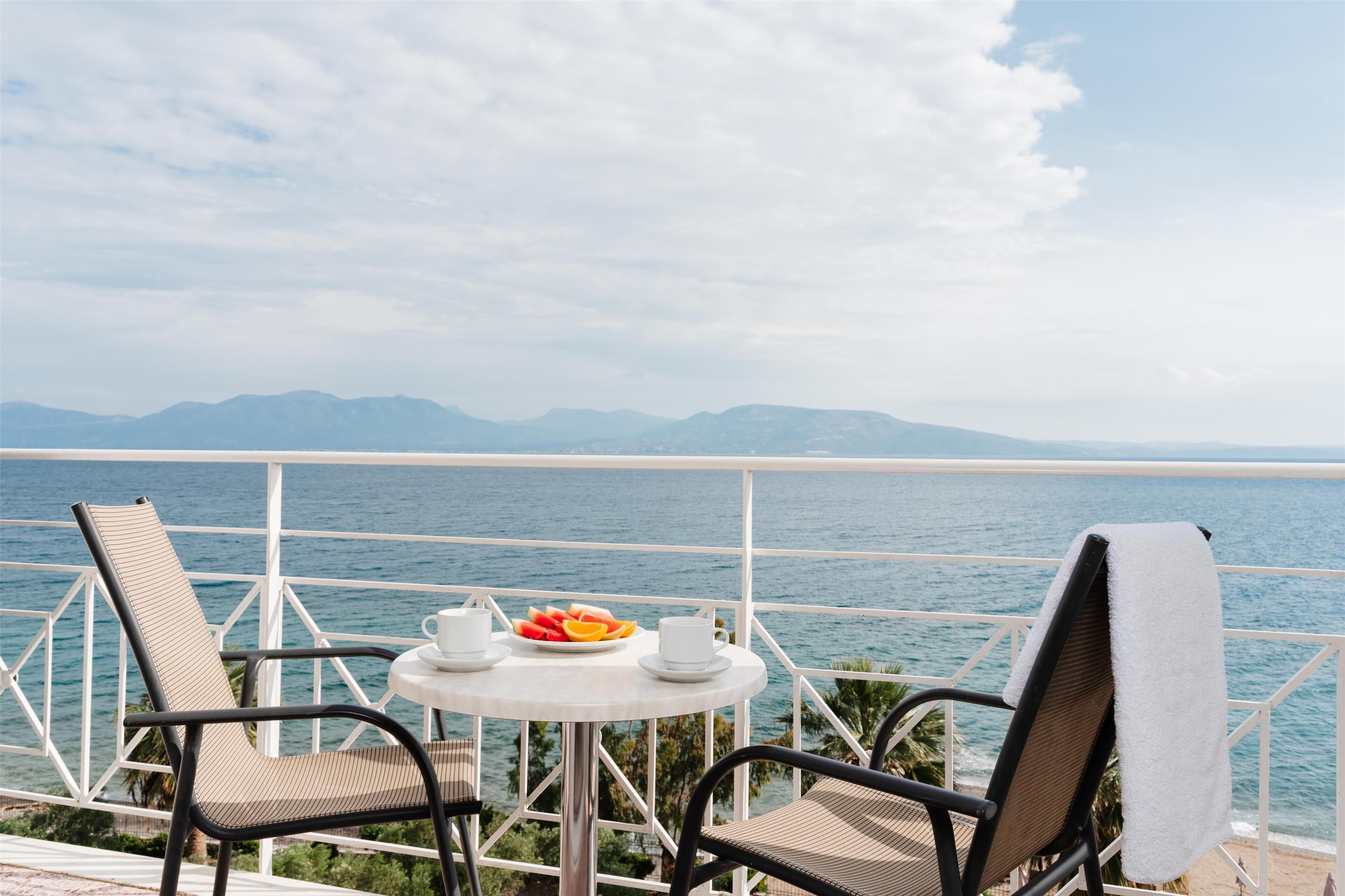 A balcony with two chairs and a table, overlooking a body of water and distant mountains.