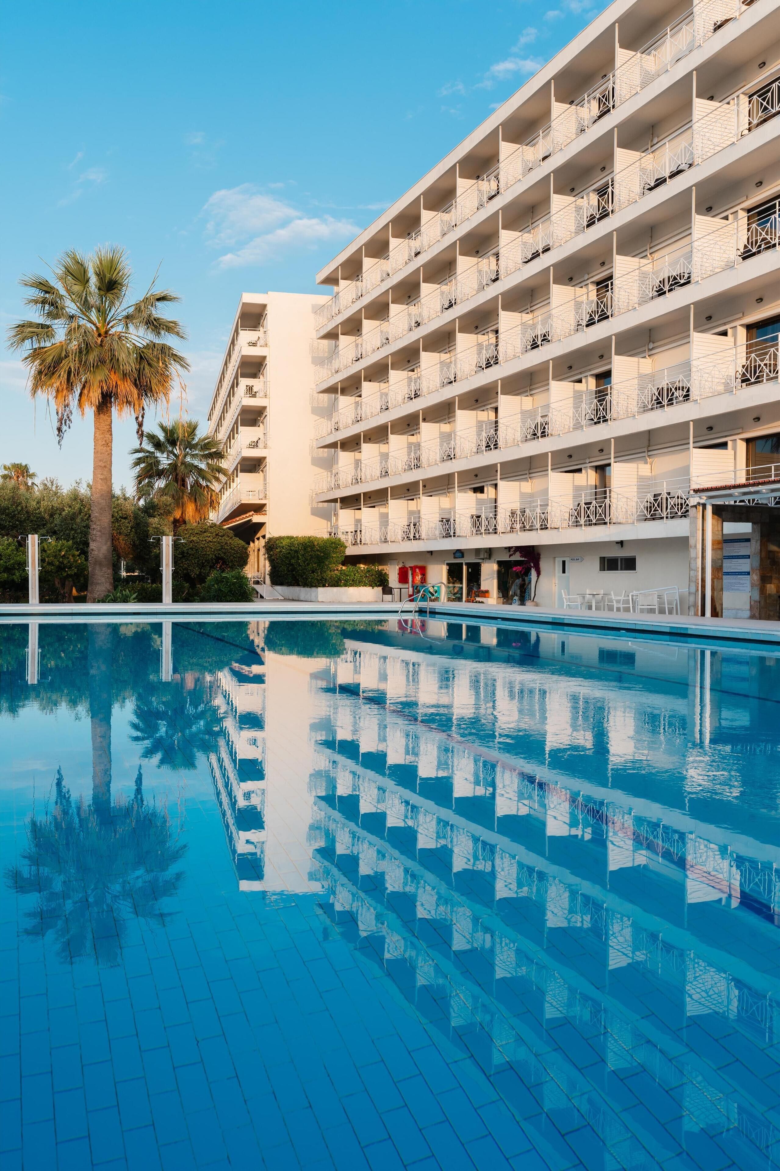 Ein modernes Hotel mit großem Pool, mehreren Balkonen und Palmen.