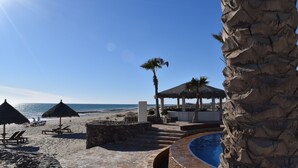 A beach resort with a pool, lounge chairs, and a thatched-roof pavilion. - Luna Blanca by Kivoya (Puerto Peñasco)