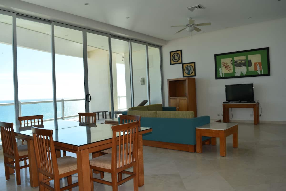 A spacious living room with a glass sliding door leading to a balcony, a television, and a sofa.