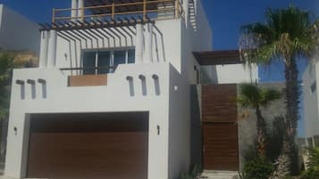 A modern two-story house with a garage, a wooden door, and a pergola on the upper floor.