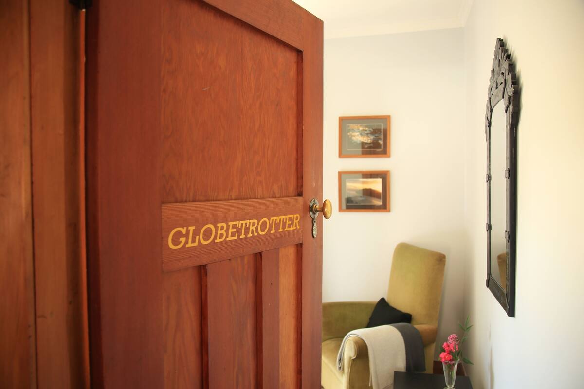 A wooden door with a nameplate reading "GLOBETROTTER" and a room with a chair and a vase of flowers.