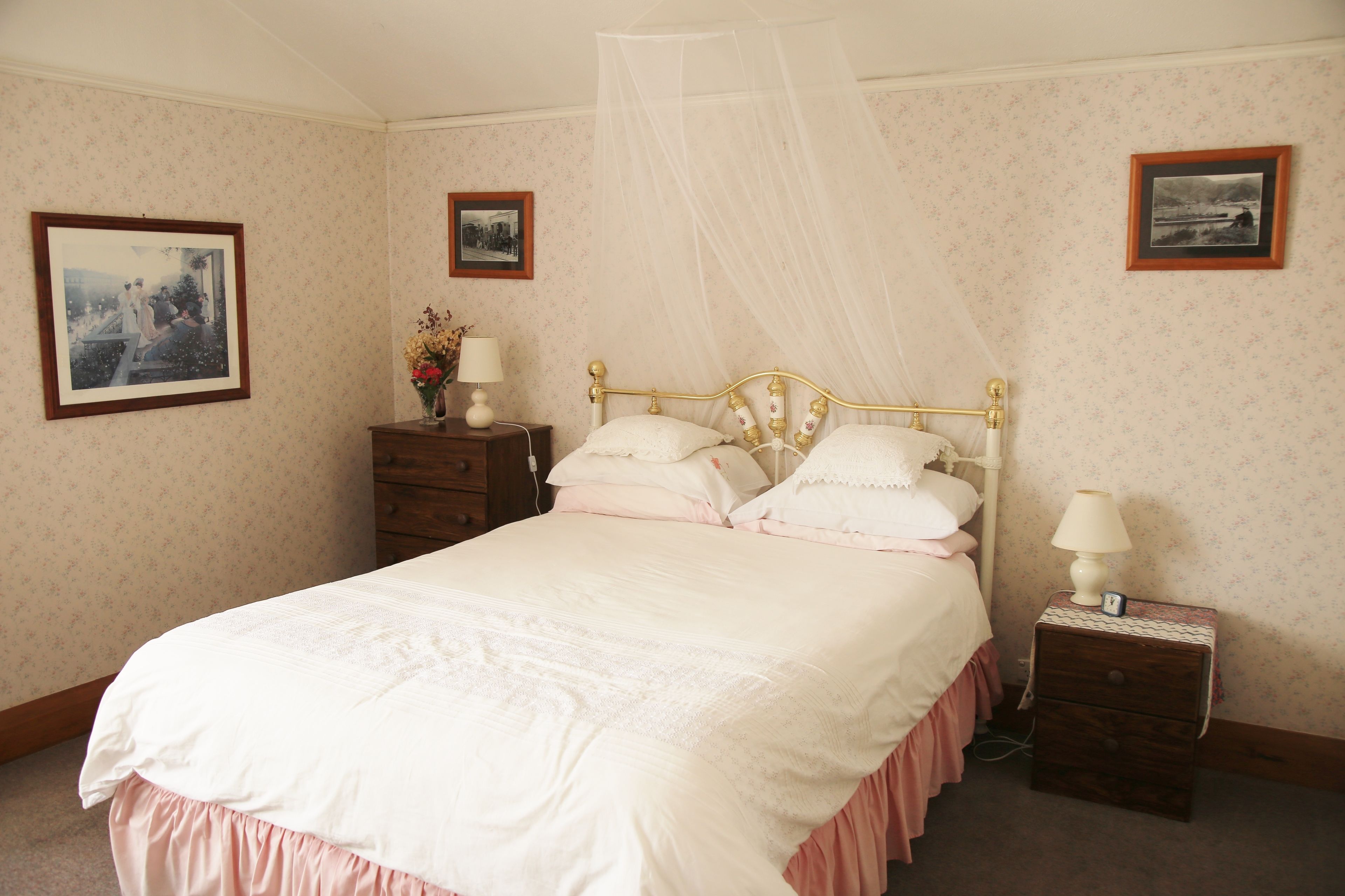 A neatly made bed with a canopy, a bedside table with a lamp, and two framed pictures on the wall.