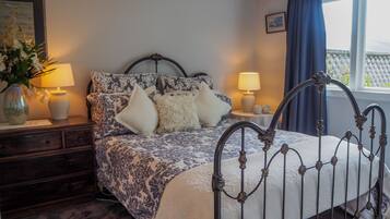 Quarto com cama, mesas de cabeceira, abajur, um vaso com flores e janela com cortinas.