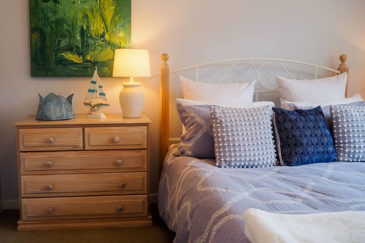 A bedroom with a bed, a nightstand, a lamp, a decorative sailboat, and a painting on the wall.