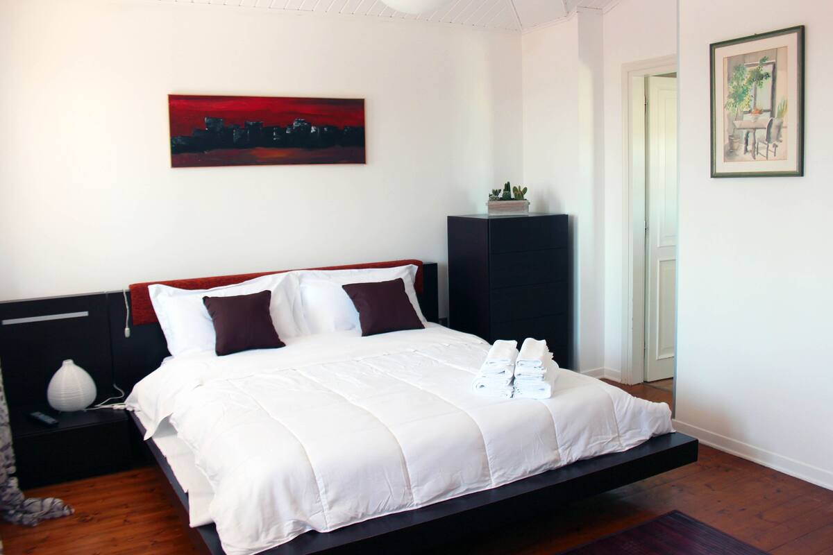 A modern bedroom with a bed, a nightstand, a wall-mounted painting, and a door.