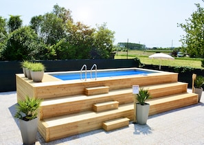 A wooden swimming pool with steps and two ladders, surrounded by potted plants and a clear view of the sky and greenery in the background. - Villa Roma Bed and Breakfast (Jesolo)