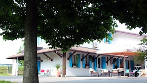 A building with a covered patio area, outdoor seating, and a large tree in the foreground.