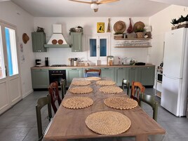 Una cucina moderna con mobili verdi, un tavolo da pranzo in legno con sottopiatti intrecciati e un frigorifero bianco.