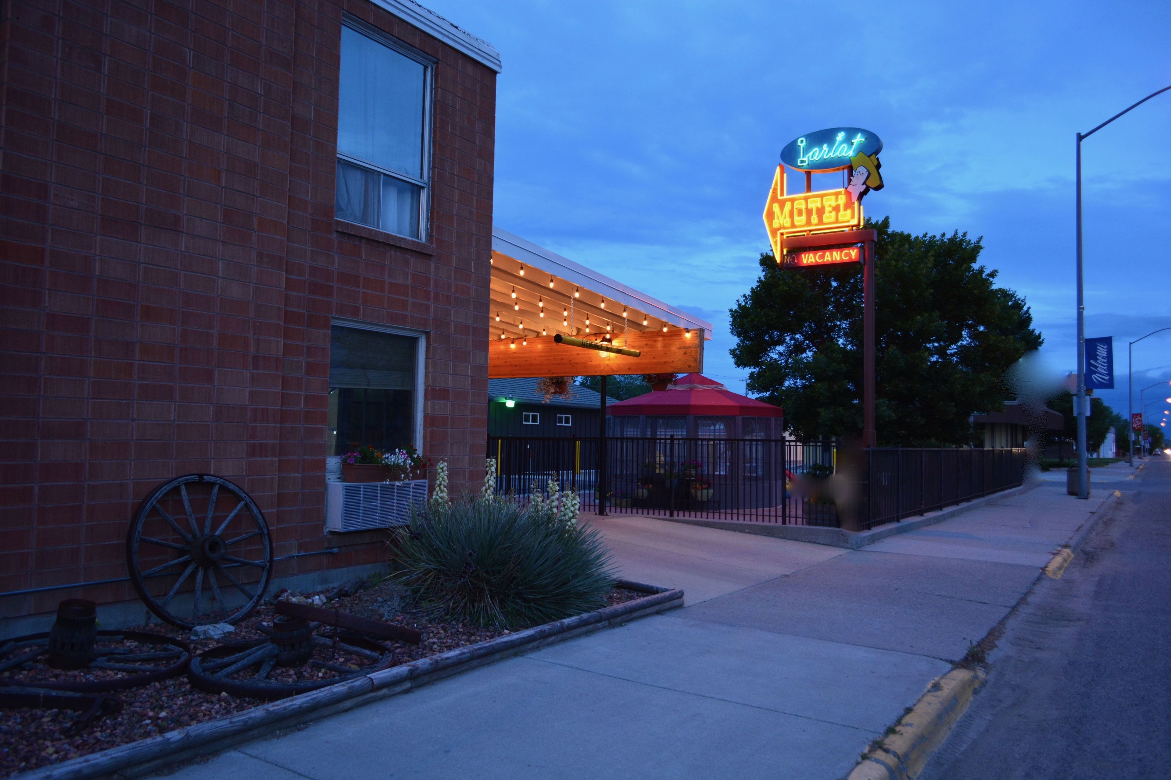 Un motel con un letrero de neón, una zona de estar al aire libre techada y una fachada de ladrillo.