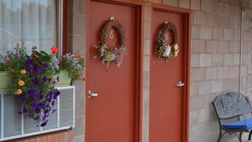 Dos puertas con coronas decorativas, una ventana con un balcón de flores y un banco en el exterior.