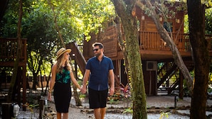 A couple walking on a gravel path surrounded by trees and wooden structures.