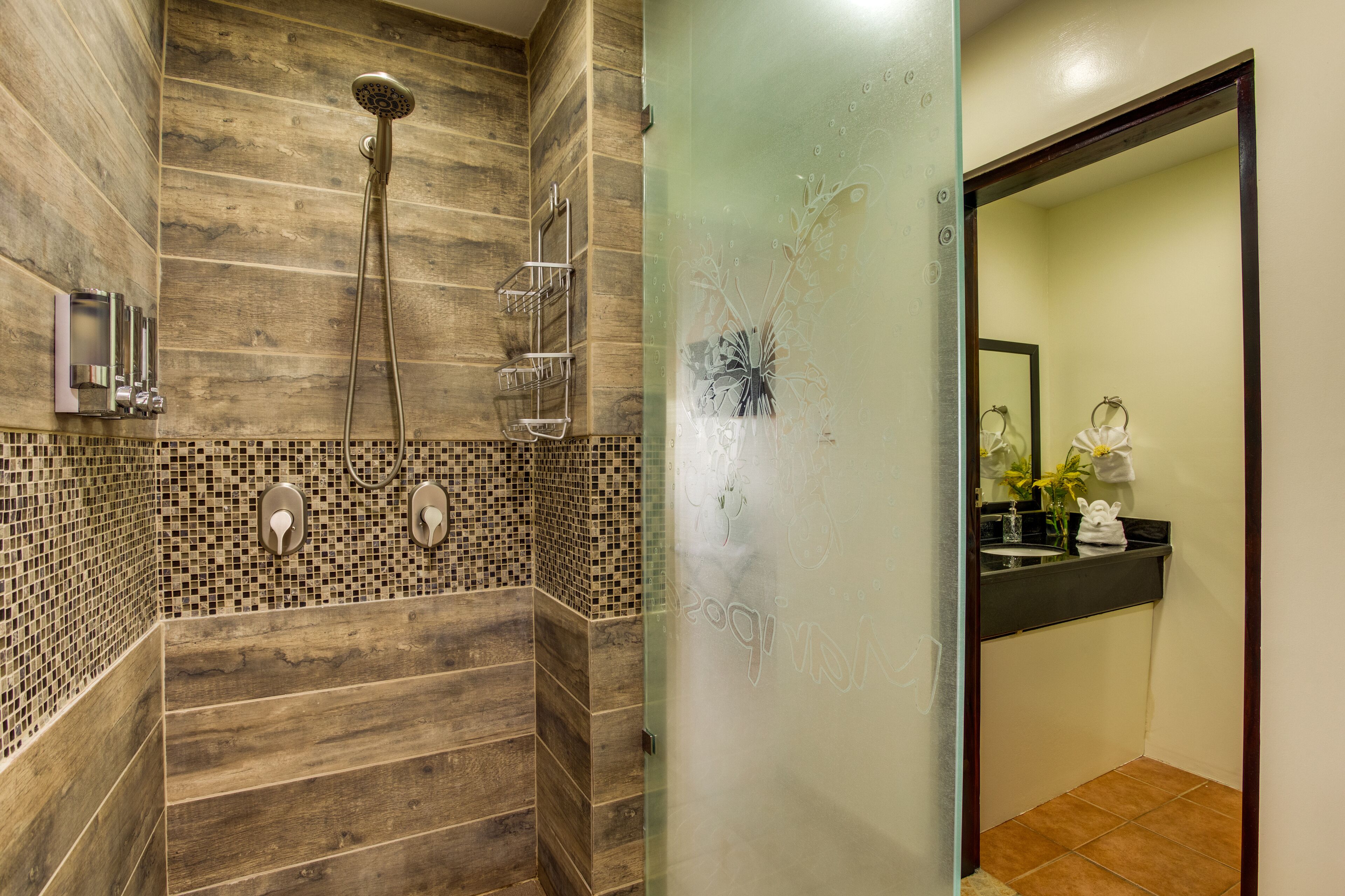 A bathroom with a wooden shower enclosure, a glass partition, and a sink with a mirror.
