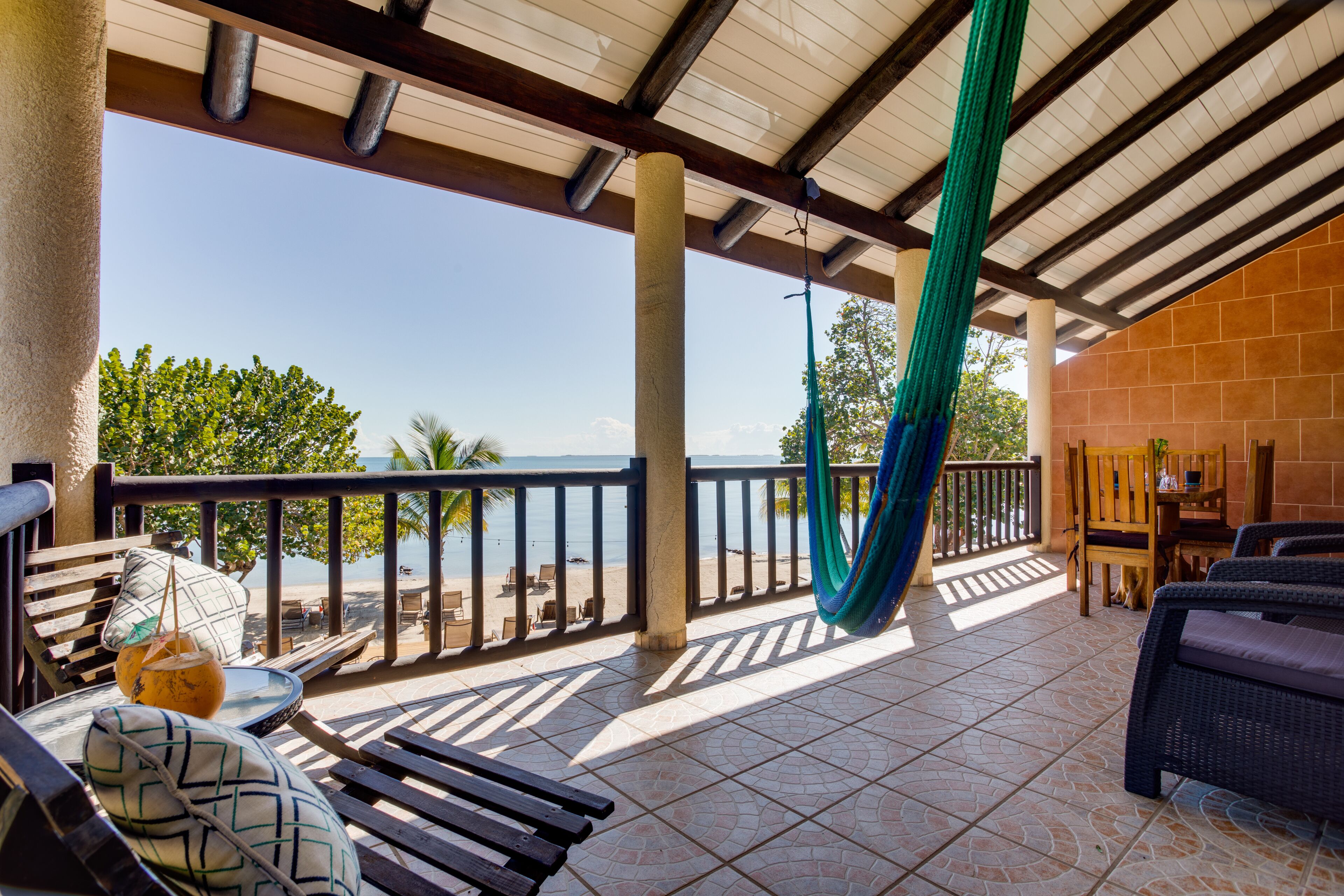 A covered outdoor area with a hammock, seating, and a view of the beach.