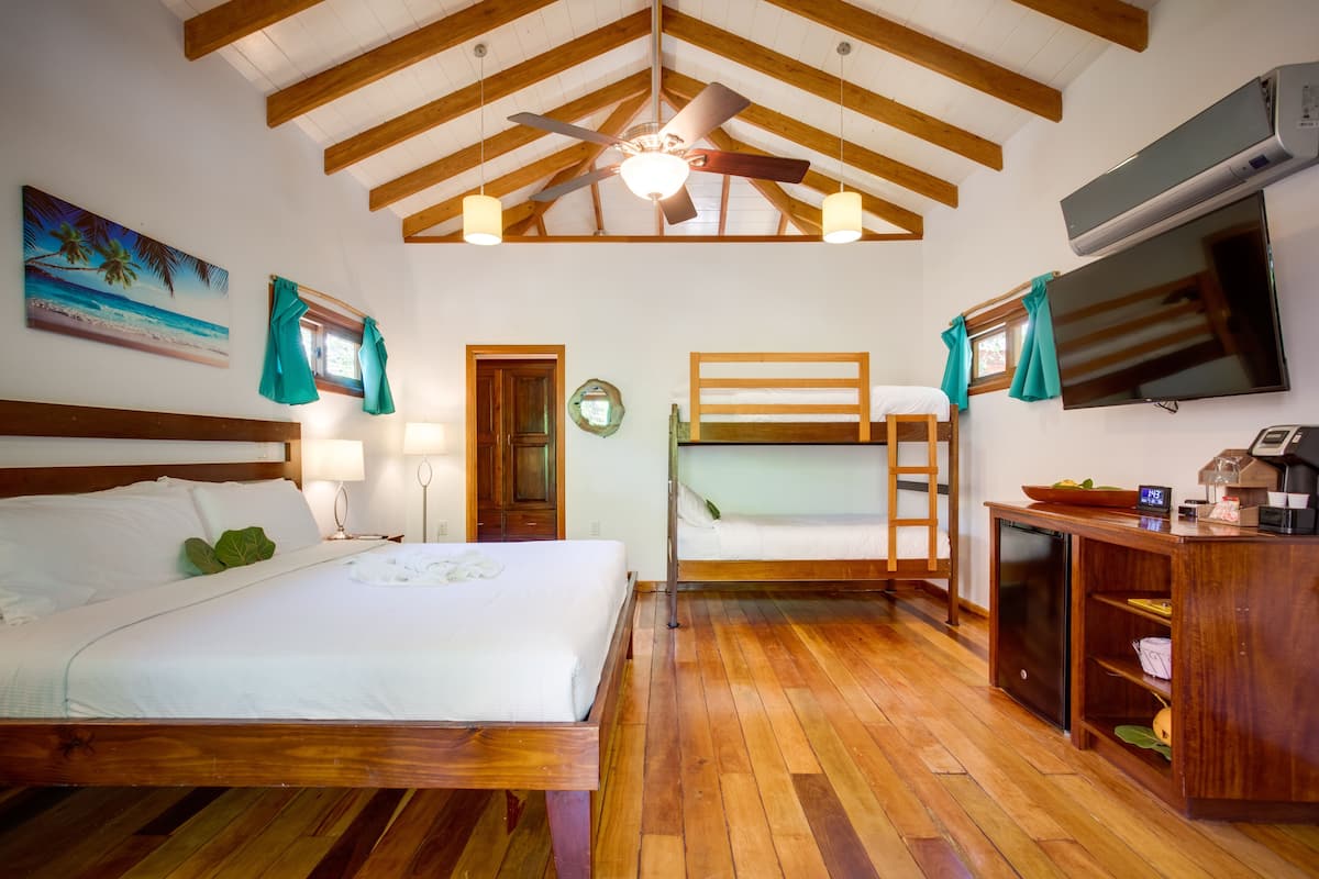 Una habitación con techo de madera, cama, escritorio, televisor y literas.