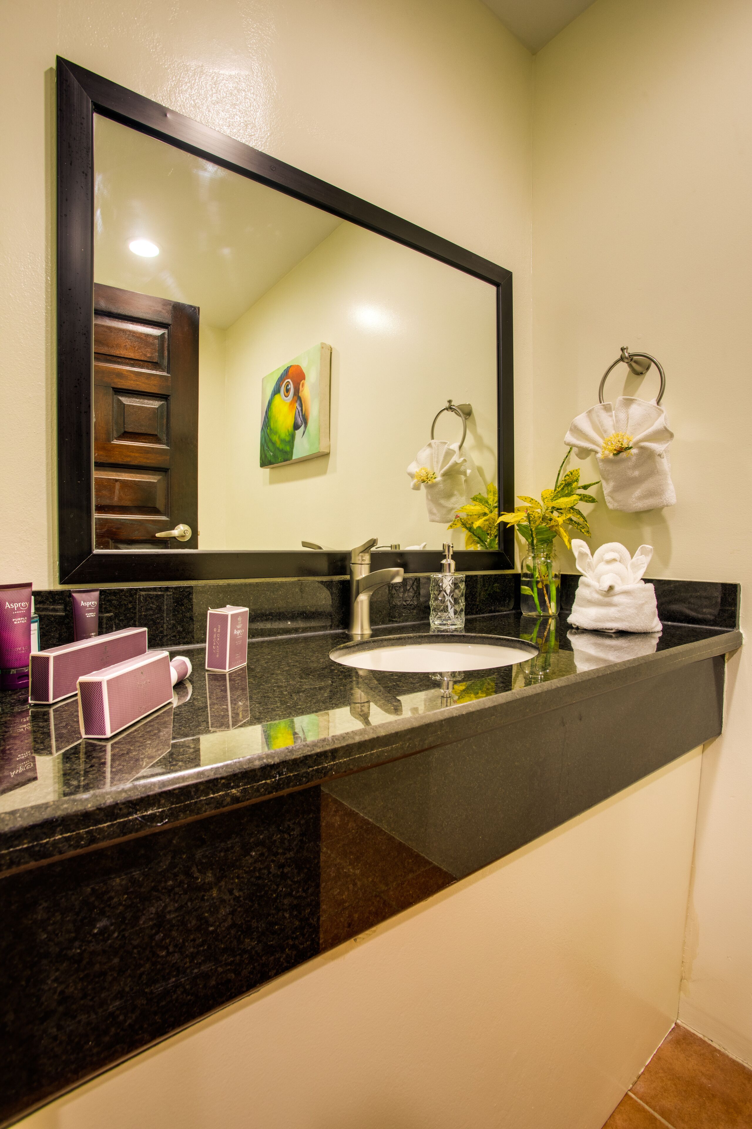 A bathroom with a large mirror, a sink, and a vanity area. There are towels hanging on the wall and a vase with flowers on the counter.