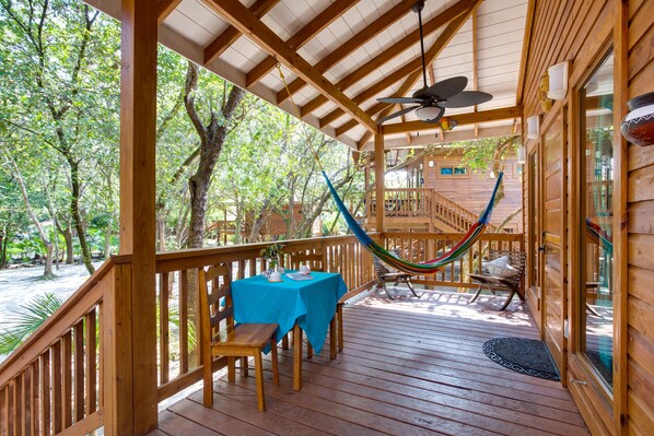 A wooden deck with a table and chairs, a hammock, and a view of the surrounding trees.